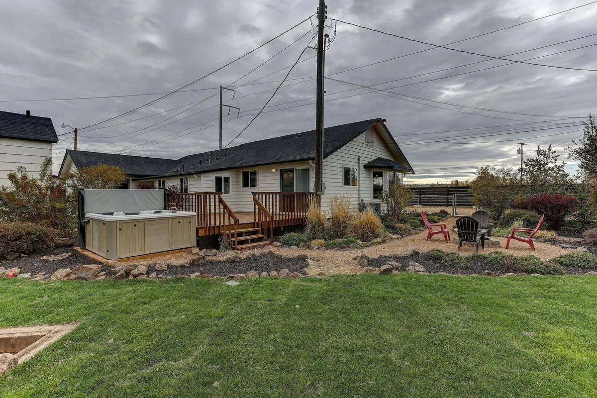 This exterior image features a cozy deck, a steaming hot tub, a fire pit gathering area, and a landscaped garden. The scene is vibrant with signs of social activity—perfect for al fresco dining, barbecues, and group relaxation through every season.