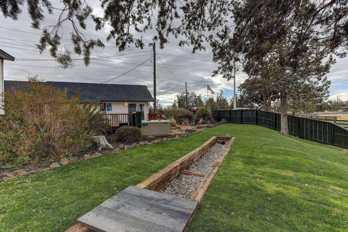 A beautifully manicured lawn and landscaped garden stretch out from a patio with inviting outdoor seating. The scene captures a peaceful backyard perfect for games, gatherings, and soaking in the beauty of changing seasons. The sunset glow enhances the atmosphere of serenity and joy.