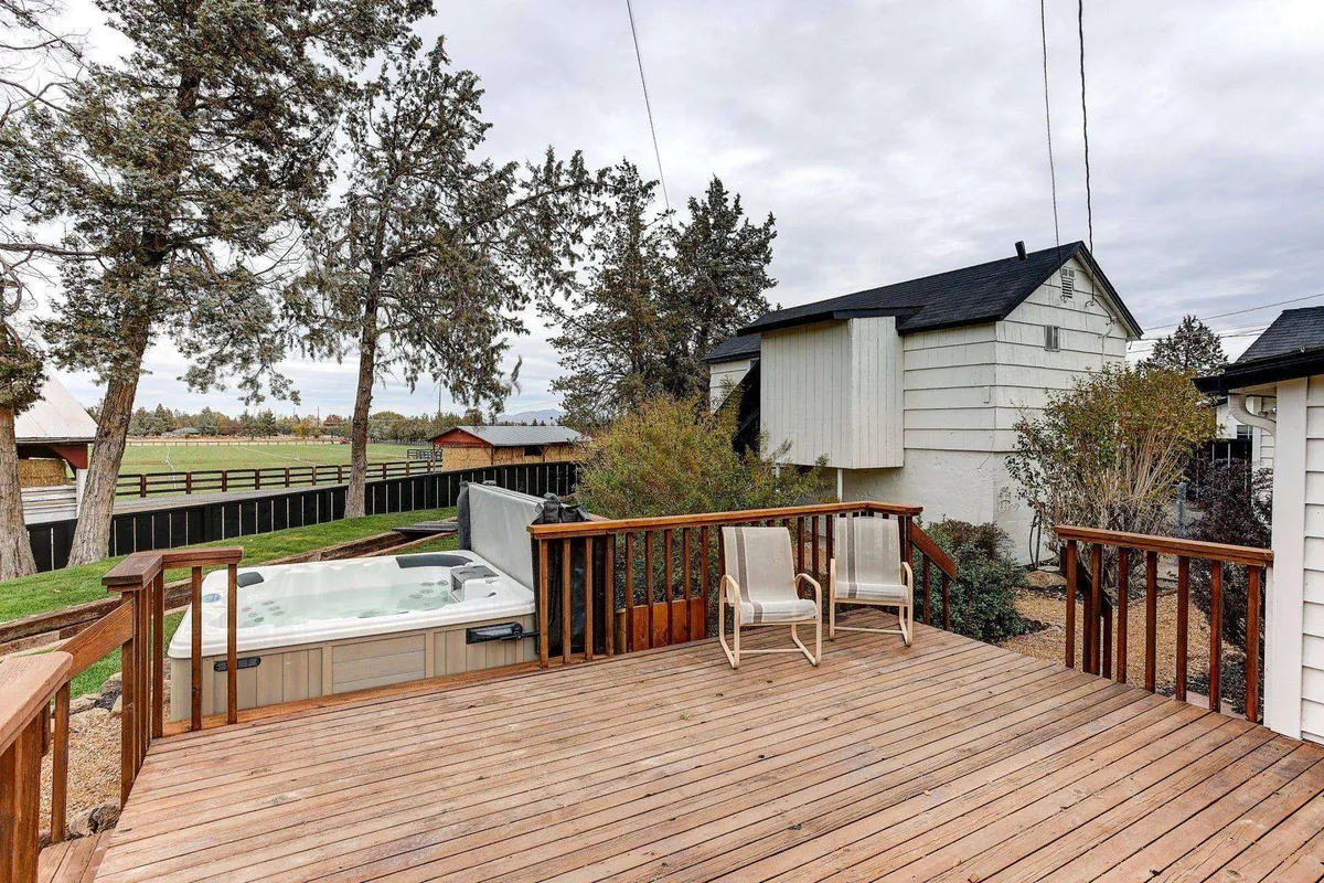 This image shows a tranquil outdoor deck with a hot tub nestled among trees and a fenced area. The deck offers comfortable seating and a relaxing atmosphere, ideal for enjoying sunsets or stargazing. The space is intimate, suggesting warmth and connection with nature throughout the seasons.
