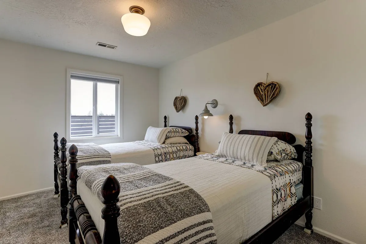 A cozy guest room with two neatly made twin beds, a window framing a peaceful view, and charming decorative heart accents that create a welcoming and homey feel.
