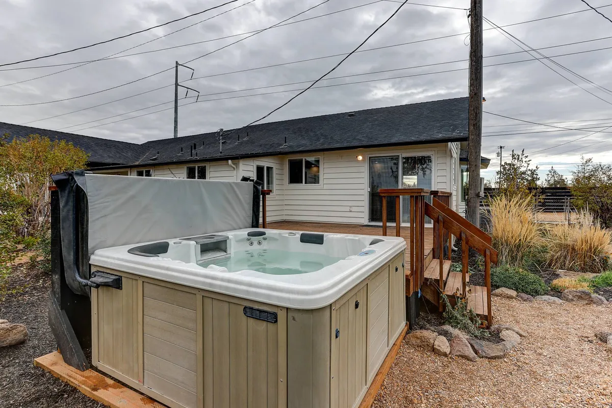 An inviting outdoor deck featuring a private hot tub surrounded by lush greenery and plants. The area is set up for relaxation, with views of the landscape stretching into the distance, making it a perfect spot for unwinding after a day of adventure or stargazing with family.