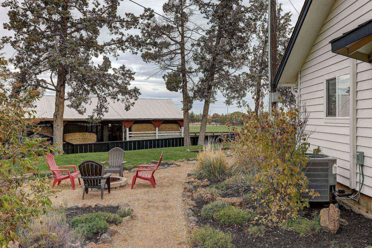 An inviting outdoor fire pit seating area beside a rustic barn structure and a landscaped garden. The setting is relaxed, encouraging communal gatherings and enjoying the great outdoors after a day full of adventure.